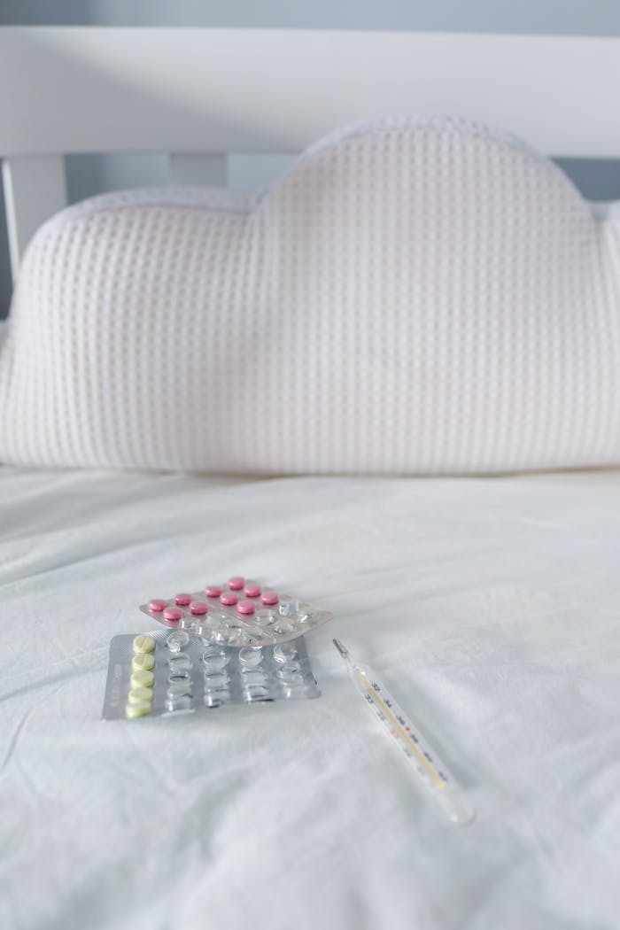 Blister packs of pills and a thermometer on a white bed, symbolizing flu treatment at home.