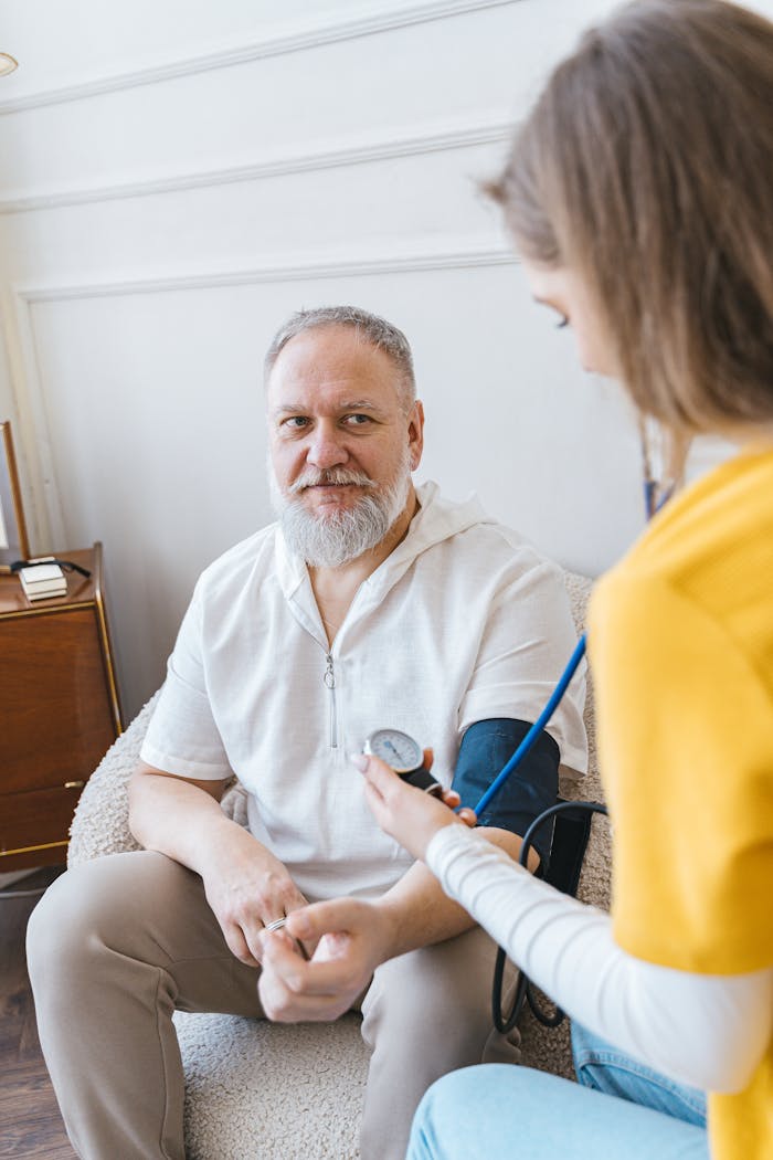 services-04 A healthcare worker takes the blood pressure of an elderly man using a monitor in a cozy indoor setting.